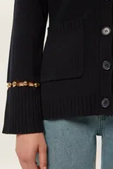 Cárdigan de punto color azul marino, con escote en V, cierre frontal con botones al tono y bolsillos de parche. Presenta mangas largas con aberturas decoradas con cuentas doradas en los puños.