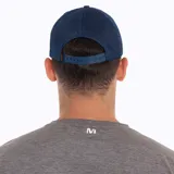 Gorra tipo trucker color azul, con panel frontal y visera de tela técnica, y paneles laterales y traseros de malla transpirable. Presenta un parche circular bordado en el frente con el logo de Merrell y un diseño de montaña.