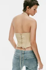 Top estilo corsé color beige, con escote recto, cuello halter y bajo asimétrico. Presenta costuras estructuradas frontales.