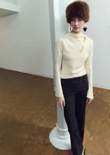Blusa de manga larga en color crema, confeccionada en poliéster. Presenta un diseño de cuello alto con un sutil detalle de abertura frontal y corte recto.