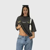 Remera de corte oversize con efecto acid wash en color gris oscuro. Presenta estampado gráfico en color amarillo en el frente con el logo de la marca y detalles de texto.