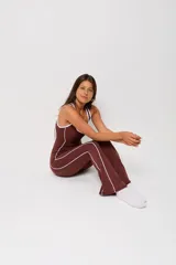Mono deportivo de una pieza color marrón, con diseño ajustado, escote redondo y tirantes anchos. Presenta líneas laterales blancas en contraste que recorren la prenda desde el escote hasta el ruedo.