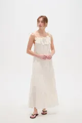 Vestido largo de algodón color blanco, con tirantes finos ajustables con lazos en los hombros, escote recto decorado con apliques florales tridimensionales, cordón ajustable en la cintura y falda larga con volados horizontales.