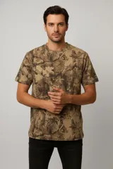 Remera de manga corta con cuello redondo, confeccionada en algodón con estampado tipo camuflado de hojas en tonos marrones y verdes.