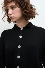 Camisa negra de tejido de punto acanalado, con cuello tipo polo y botones blancos.