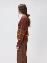 Sweater clásico de punto cable con cuello redondo a la base, mangas largas y fit al cuerpo. De color marrón con franjas horizontales violetas y amarillas, cuenta con el cuello, puños y ruedo acanalados, además de un pequeño logo bordado en el pecho.