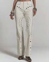 Jeans de corte recto color crudo con apliques de tachas metálicas plateadas distribuidas en patrones geométricos.
