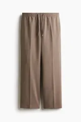 Pantalón de corte relajado y pierna recta, confeccionado en tejido suave de color marrón. Presenta cintura elástica con cordón de ajuste, pliegues frontales y traseros, bolsillos laterales y un bolsillo posterior insertado.