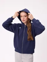 Canguro azul marino con cierre frontal, capucha y bolsillos laterales. Presenta un parche bordado con el número 85 en color celeste y blanco en la manga.