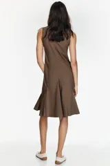 Vestido midi camisero color marrón, sin mangas, con cuello solapa y cierre frontal de botones. Presenta bolsillos delanteros con solapa y diseño con pliegues en el bajo.