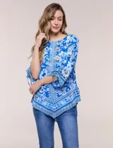 Blusa de gasa azul con estampado floral y geométrico estilo pañuelo, escote redondo, mangas tres cuartos amplias con jareta ajustable y ruedo asimétrico en punta.