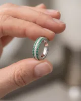 Anillo de plata con diseño de tres hileras, con circones blancos en el centro y piedras verdes en los laterales.
