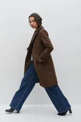 Tapado de lana color marrón con silueta entallada. Presenta solapas clásicas decoradas con un volado en contraste de color azul oscuro, cierre frontal con un botón y bolsillos laterales. Las mangas cuentan con detalles de botones en los puños.