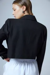 Saco sastrero corto a la cintura, color negro, con cierre frontal de un botón grabado, solapas clásicas, bolsillo ojal en el delantero, chapa metálica con logo en el pecho y bordado decorativo en la manga.