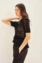 Camisa liviana negra tejida en punto desagujado con cuello en rib y cartera con botones símil nacar en el delantero.