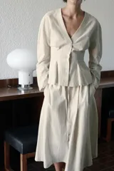 Blusa entallada de lino color beige con finas rayas verticales rosadas, escote en V, manga larga y cierre frontal con botones.