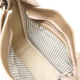 Cartera de cuero color taupe con diseño estructurado, correa ancha ajustable con ojales metálicos decorativos y placa metálica con logo en el frente.