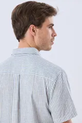 Camisa de manga corta confeccionada en mezcla de lino y algodón, con diseño de rayas verticales en tonos celeste y blanco. Cuenta con cuello camisero, botonadura frontal y bordado sutil en el pecho.