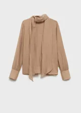 Blusa color beige con textura, cuello alto con lazo, mangas largas con puños abotonados y corte recto.