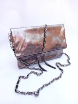 Cartera plateada tipo bandolera con solapa y cierre magnético. Tiene una cadena corta y una cadena larga.