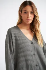 Cárdigan de tejido liviano con textura acanalada, cuello en V y cierre frontal con botones. Presenta mangas largas y un diseño clásico con detalle de grifa en cuero.