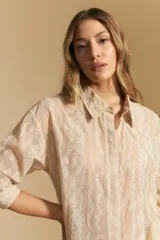 Camisa blanca de manga larga con textura calada o bordada, cuello camisero y corte holgado.