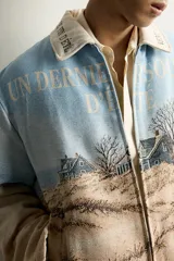 Cazadora relaxed fit de tejido jacquard ligeramente acolchado, con estampado de paisaje costero y texto "Un dernier souffle d'été". Cuenta con cuello solapa con inscripción, manga larga, bolsillos de vivo en la cadera y cierre frontal con cremallera.