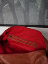 Bolso de viaje tipo weekender de cuero color tostado con asas y detalles en marrón oscuro, herrajes metálicos y bolsillo frontal con cierre.