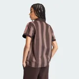 Camiseta de fútbol Adidas de manga corta, color marrón con diseño de rayas verticales oscuras. Presenta cuello polo con escote en V, el logo clásico de la marca bordado en el pecho junto con la inscripción "adidas" en gran tamaño al frente, y las franjas características de la marca en los hombros.
