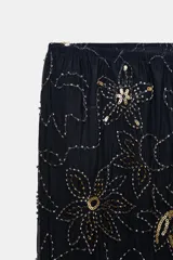 Pantalón de tiro alto, pierna recta y forro interior tipo shorts. Confeccionado en tejido negro con bordado floral en lentejuelas y abalorios dorados.