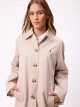 Gabardina de corte clásico en color azul marino, con cierre frontal de botones, cuello camisero y bolsillos laterales. Presenta un diseño minimalista con un pequeño bordado en el pecho.
