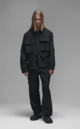 Chaqueta técnica liviana de microfibra con acabado mate, diseño con mangas desmontables que permiten convertirla en chaleco. Cuenta con cuello tipo camisa, cierre frontal oculto, cuatro bolsillos frontales de gran tamaño y puños elásticos. Incluye logo bordado en relieve en el pecho.