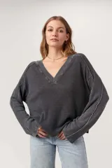 Remera de manga larga con escote en V amplio, confeccionada en tejido térmico suave con lavado burnout que le da un acabado vintage. Presenta costuras expuestas y bordes sin rematar, con mangas levemente acampanadas.