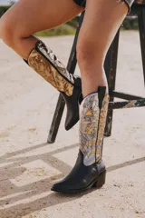 Bota texana de cuero vacuno negro con detalles bordados en dorado y plateado en la caña. Tiene taco de madera con folia de cuero de 5cm, entre suela de goma de 1cm, inclinación de horma de 4cm, altura de caña de 31cm y cierre YKK del lado interno. La horma es de punta fina, ancha y cómoda.