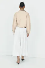 Camisa de popelín color beige con cuello solapa y lazada frontal en contraste con estampado de rayas marrones. Presenta mangas largas abullonadas con puños elásticos, bolsillos con solapa en el pecho y bajo elástico.