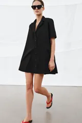 Vestido corto de algodón con cuello solapa, manga corta y cierre frontal con botones. Presenta un diseño evasé con bolsillos laterales ocultos en las costuras.
