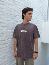 Remera oversize de manga corta, color marrón oscuro con efecto gastado (acid wash), con un logo ovalado blanco que contiene el texto "OSTEN" en el centro del pecho.