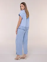 Blusa de algodón celeste con textura tramada tipo denim lavado, cuello solapa abierto en V, botones frontales y detalle de puntilla tejida al crochet en el ruedo.