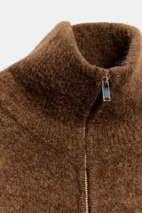Chaqueta de punto de textura suave en color marrón, con cuello alto, manga larga con puños ajustados y cierre frontal completo con cremallera metálica.