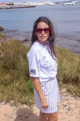 Remera blanca de algodón, de corte holgado y manga corta, con un parche rectangular bordado en la manga derecha que presenta un diseño gráfico colorido.