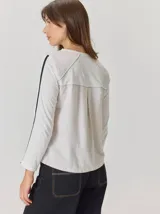 Remera de manga larga color blanco, con cuello redondo y detalle de costuras en contraste en la parte superior de los hombros.