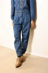 Pantalón de jean estilo gaucho, de tiro alto con pinzas frontales y cierre de botones. Presenta un corte holgado que se ajusta ligeramente en los tobillos.