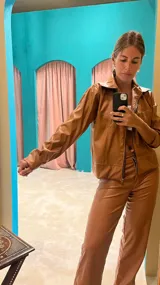 Campera marrón de cuero sintético con cierre frontal, cuello camisero y costuras decorativas en hilo blanco.