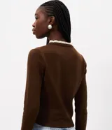 Cardigan de punto marrón de manga larga, con cierre frontal de botones y detalles de encaje blanco en el cuello redondo y los puños.