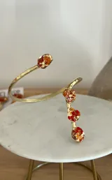 Brazalete abierto de metal dorado con acabado martillado, decorado con piedras naturales en tono turquesa con incrustaciones doradas en los extremos.