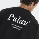Remera negra de corte boxy con costuras a la vista en contraste de color blanco. Presenta un pequeño logo estampado en el centro del pecho y una frase bordada en el bajo lateral. Posee mangas cortas y cuello redondo.
