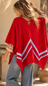 Ruana roja de lana con dos líneas horizontales blancas en la parte inferior delantera y detalles de cintas tejidas.
