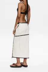 Falda pareo midi color blanco con bodoques negros a contraste y cierre con lazo en la cintura.