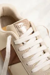 Zapatillas bajas color crema con puntera de gamuza beige, detalle de franja lateral en cuero marrón y contrafuerte en cuero metalizado color cobre.