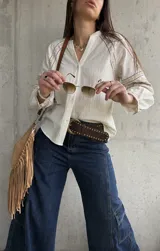 Camisa de inspiración boho de color crudo, con mangas largas abullonadas y puños decorados con detalles bordados geométricos en tonos tostados y dorados. Presenta cuello en V con cierre frontal de botones.